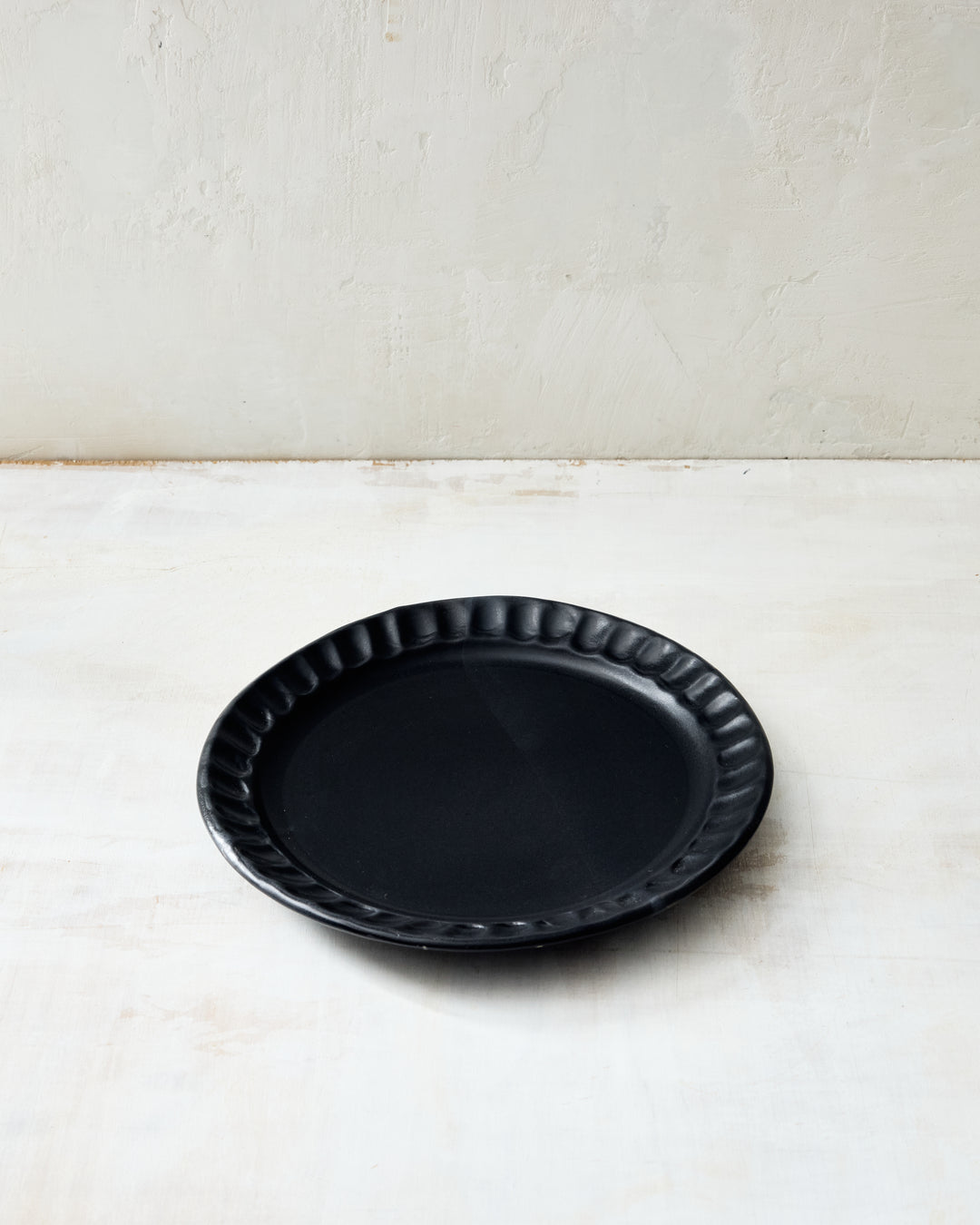 DBO HOME Nonna Salad Plate in Matte Black glaze, highlighting the sculptural fluting around the rim. A sleek, modern addition to any table, this handmade plate pairs sophistication with artisan texture.
