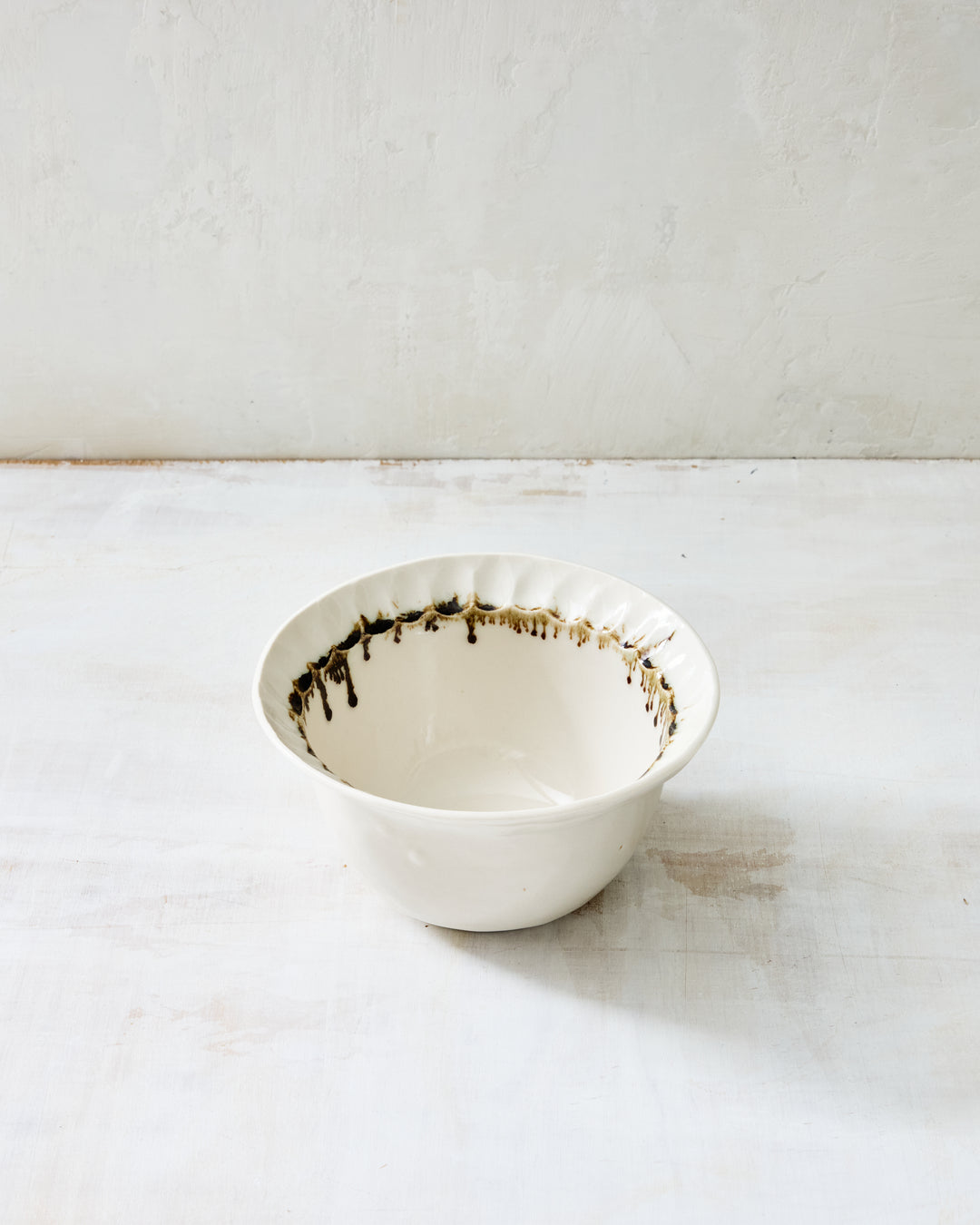 Handmade Nonna Dinner Plate by DBO HOME, crafted from creamy porcelain with a clear glaze and finished with a hand-applied bronze rim. The softly fluted edge adds quiet texture, while the bronze varies from dark espresso to warm caramel. Photographed on a whitewashed background to highlight its sculptural form and subtle sheen.
