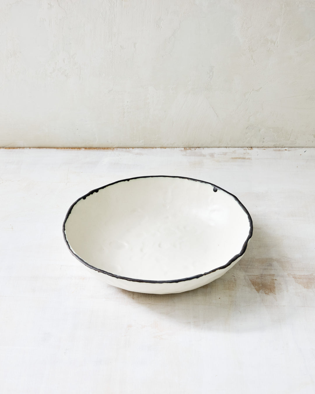 DBO HOME Pinch Everything Bowl in white porcelain with a bronze rim, photographed on a whitewashed surface. Its softly flared form and lush glaze make it perfect for generous servings or simple everyday moments.