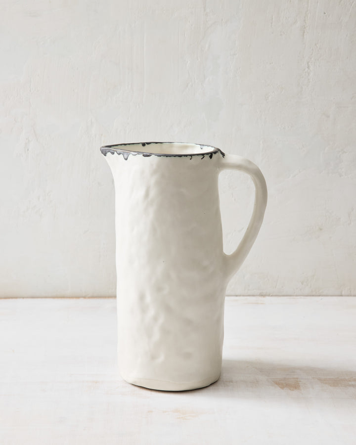 DBO HOME Pinch Pitcher in creamy porcelain with a flowing bronze-rimmed lip. This tall, hand-built ceramic pitcher features an organic silhouette and sturdy handle—ideal for water, wine, or fresh-cut stems on the table.