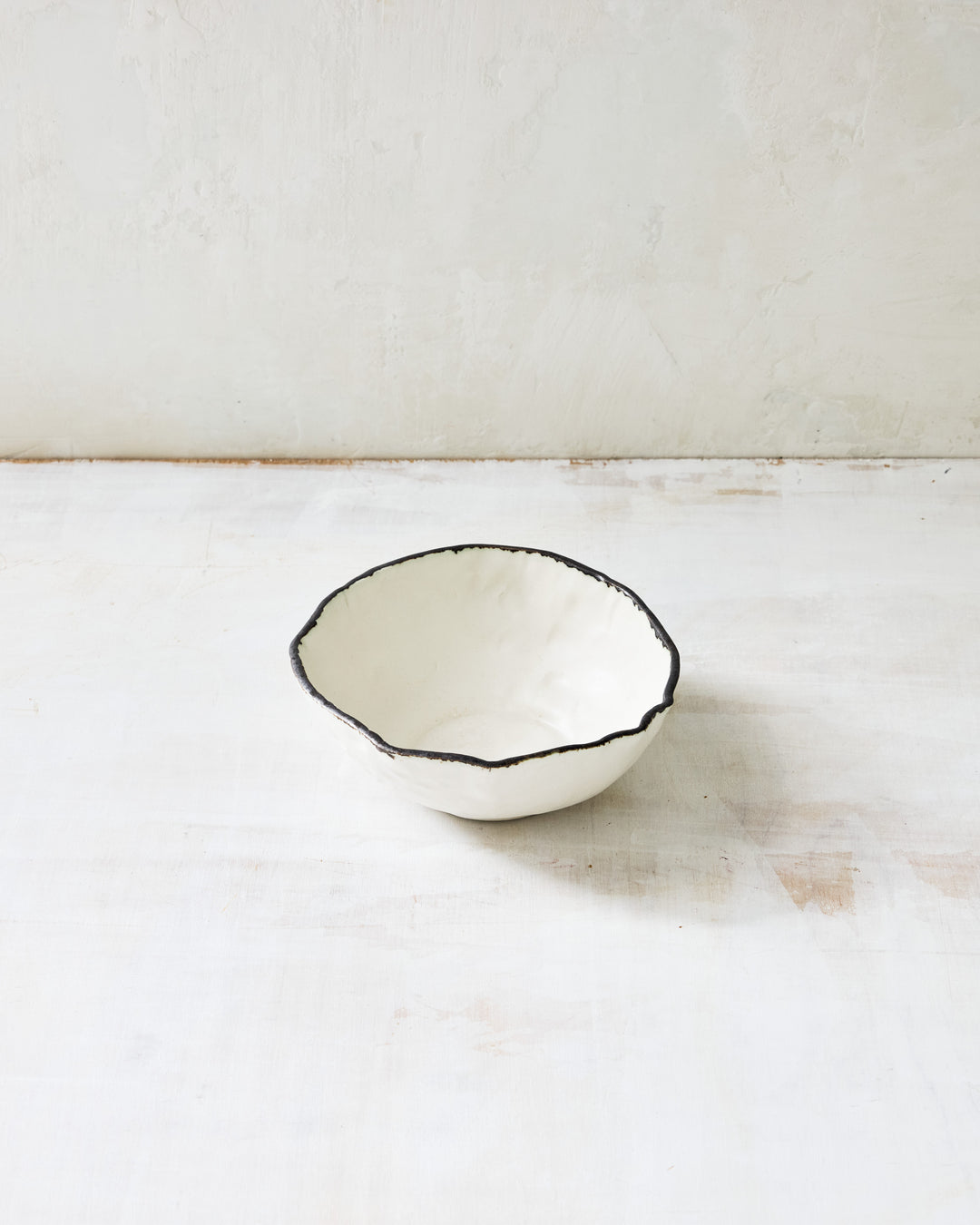 Handmade Pinch Soup Bowl by DBO HOME in white porcelain with a bronze edge. The softly uneven rim and subtle dimpled texture make this ceramic bowl ideal for soup, stews, or small salads. Photographed on a pale wood surface.
