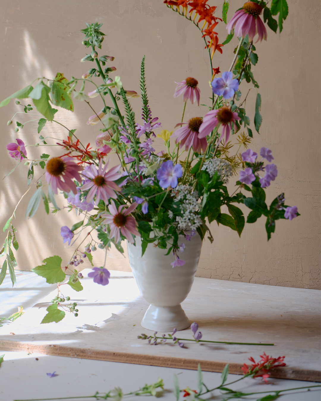 DBO HOME Bare Pedestal Vase in Snowflake porcelain, filled with a wild, seasonal arrangement by Romane Recalde of Le Jardin Flower Farm. Photographed by John Gruen in soft natural light, the vase’s smooth form anchors the airy, organic composition. [Styling: Romane Recalde; Photography: John Gruen]