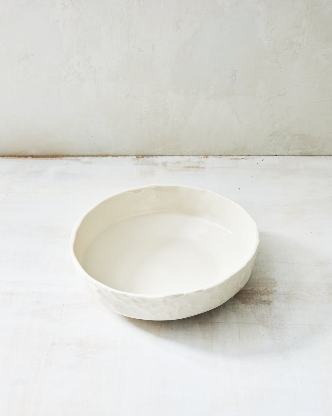 DBO HOME Stucco Everything Bowl in clear-glazed handmade porcelain with a wide, shallow form and tactile stucco-textured exterior, photographed on a whitewashed surface.