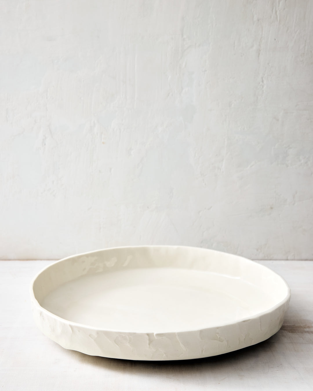 DBO HOME Stucco Serving Bowl in handmade porcelain with a wide, low-profile form and tactile stucco-textured exterior, front view photographed on a whitewashed surface.