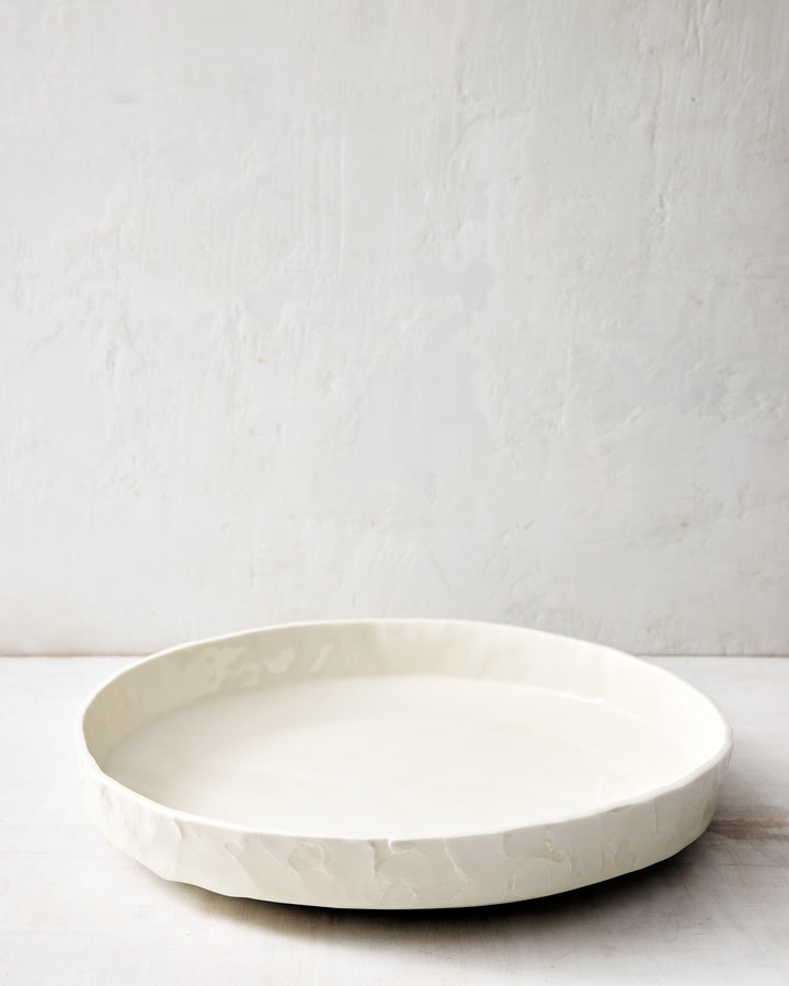 DBO HOME Stucco Serving Bowl in handmade porcelain with a wide, low-profile form and tactile stucco-textured exterior, front view photographed on a whitewashed surface.