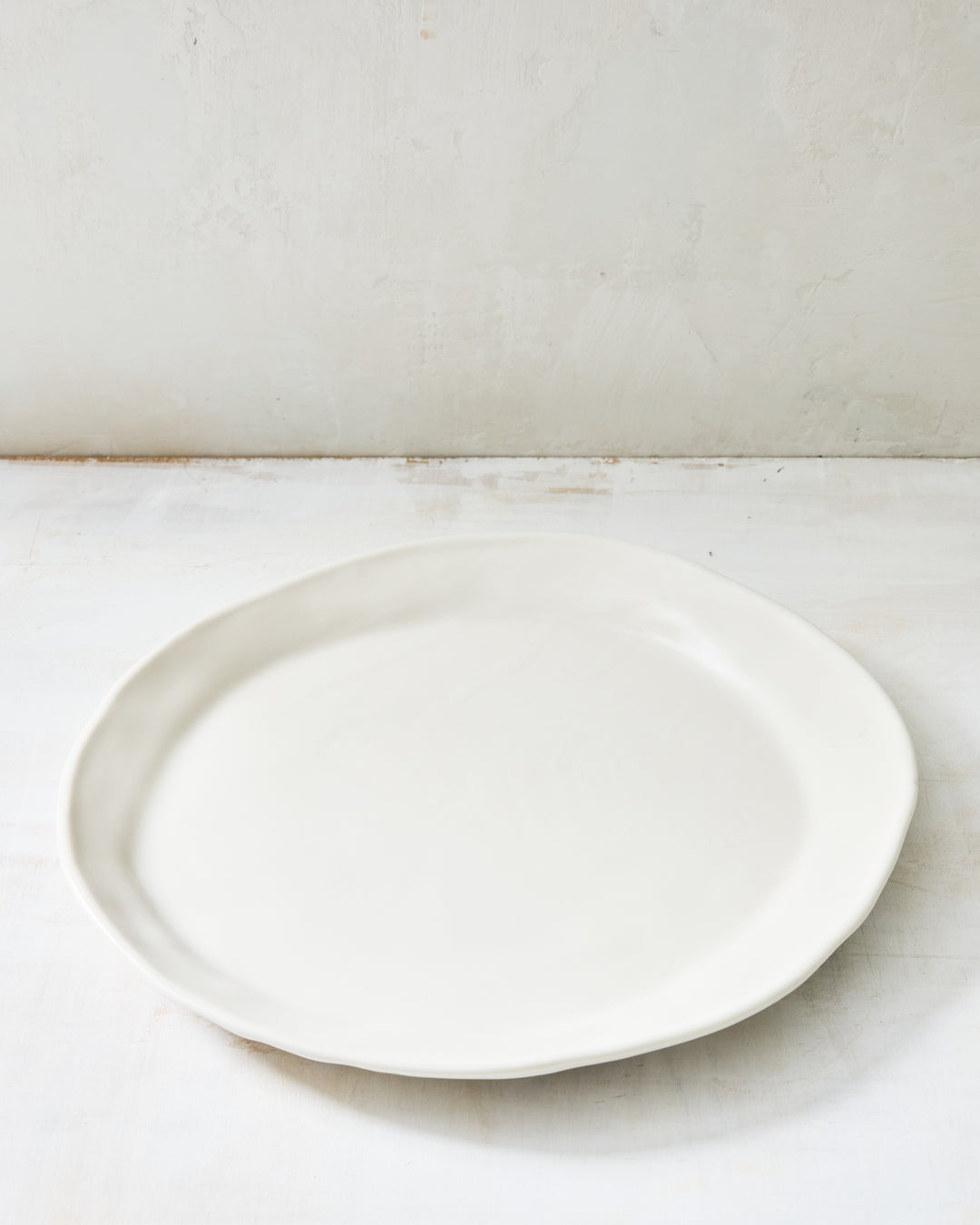 DBO HOME Wabi Dinner Plate in Foam glaze, handmade porcelain with a subtle white-on-white layered glaze and a stone-like surface texture, photographed on a whitewashed surface.