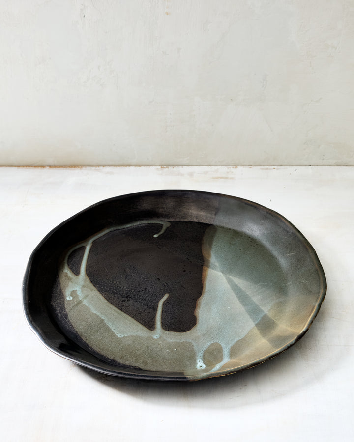 DBO HOME Wabi Dinner Plate in Granite glaze, handmade porcelain with a layered mussel and snowflake glaze and a stone-like surface texture, photographed on a whitewashed surface.