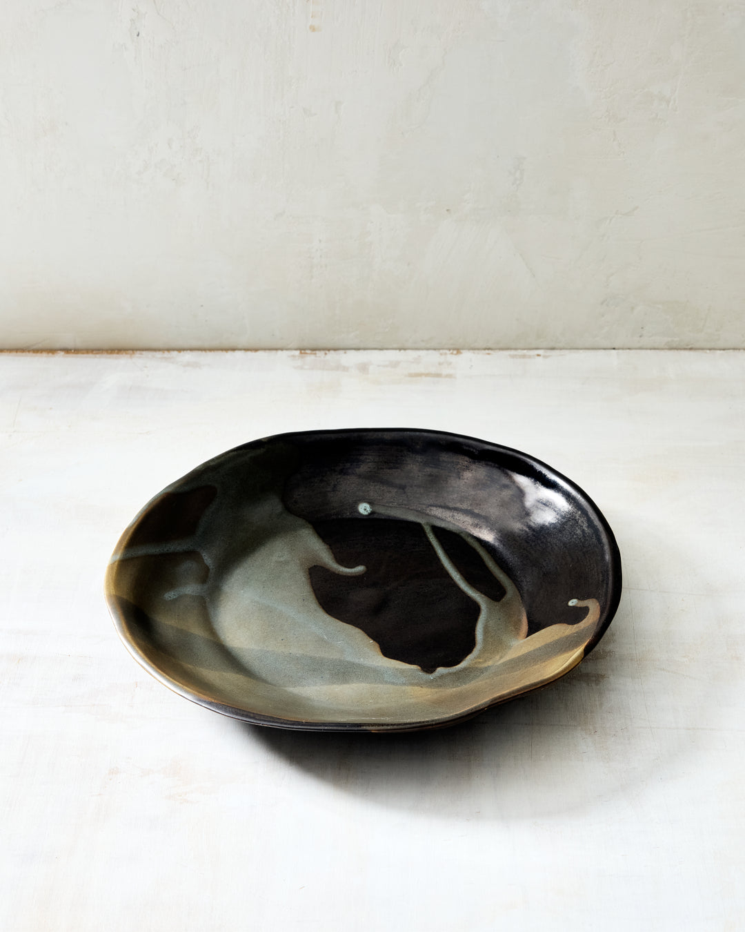 DBO HOME Wabi Pasta Bowl in Granite glaze, handmade porcelain with a wide shallow form, layered mussel and snowflake glaze, and a stone-like surface texture, photographed on a whitewashed surface.