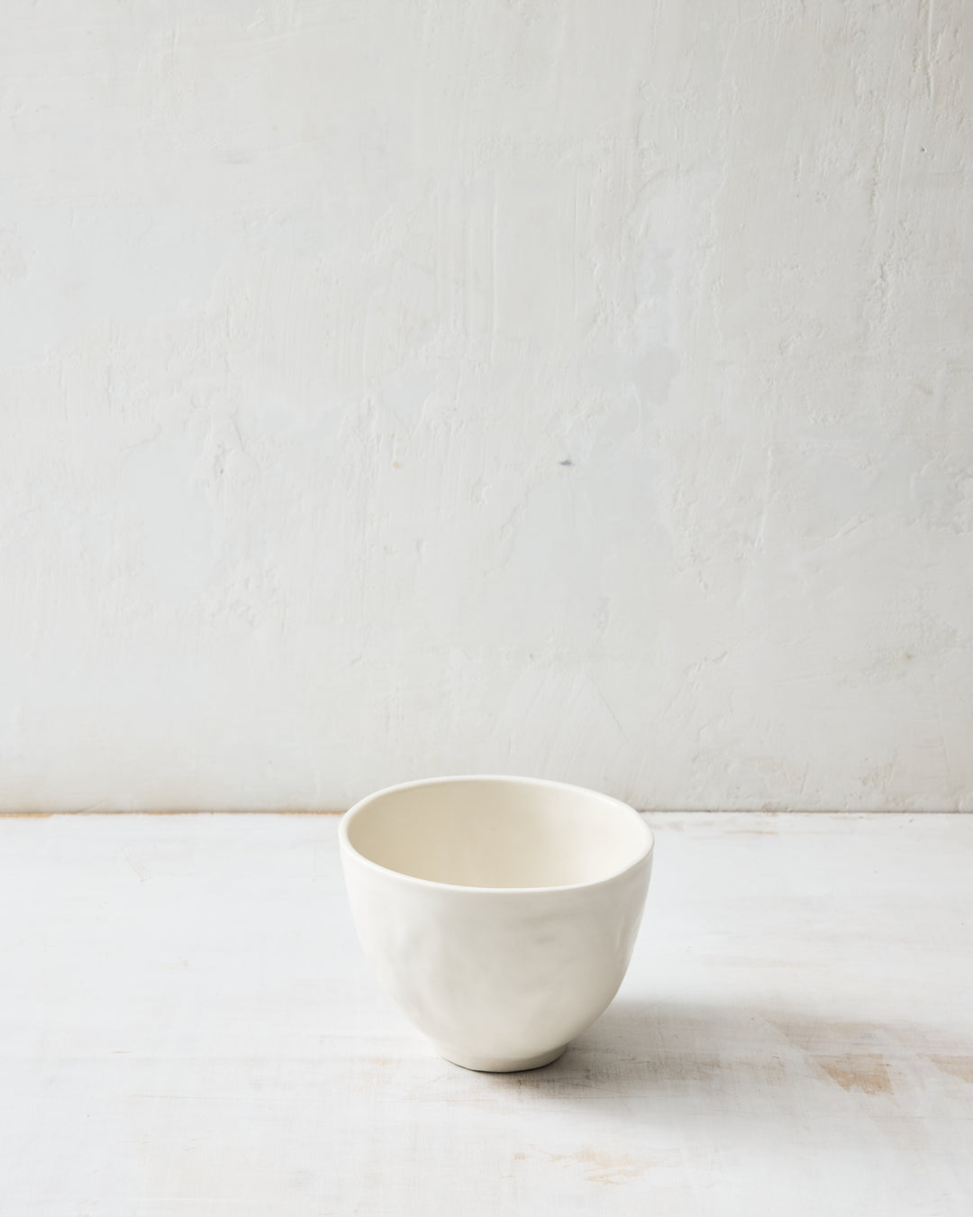 DBO HOME Wabi Rice Bowl in Foam glaze, handmade porcelain with a rounded form, subtle white-on-white layered glaze, and stone-like surface texture, photographed on a whitewashed surface.