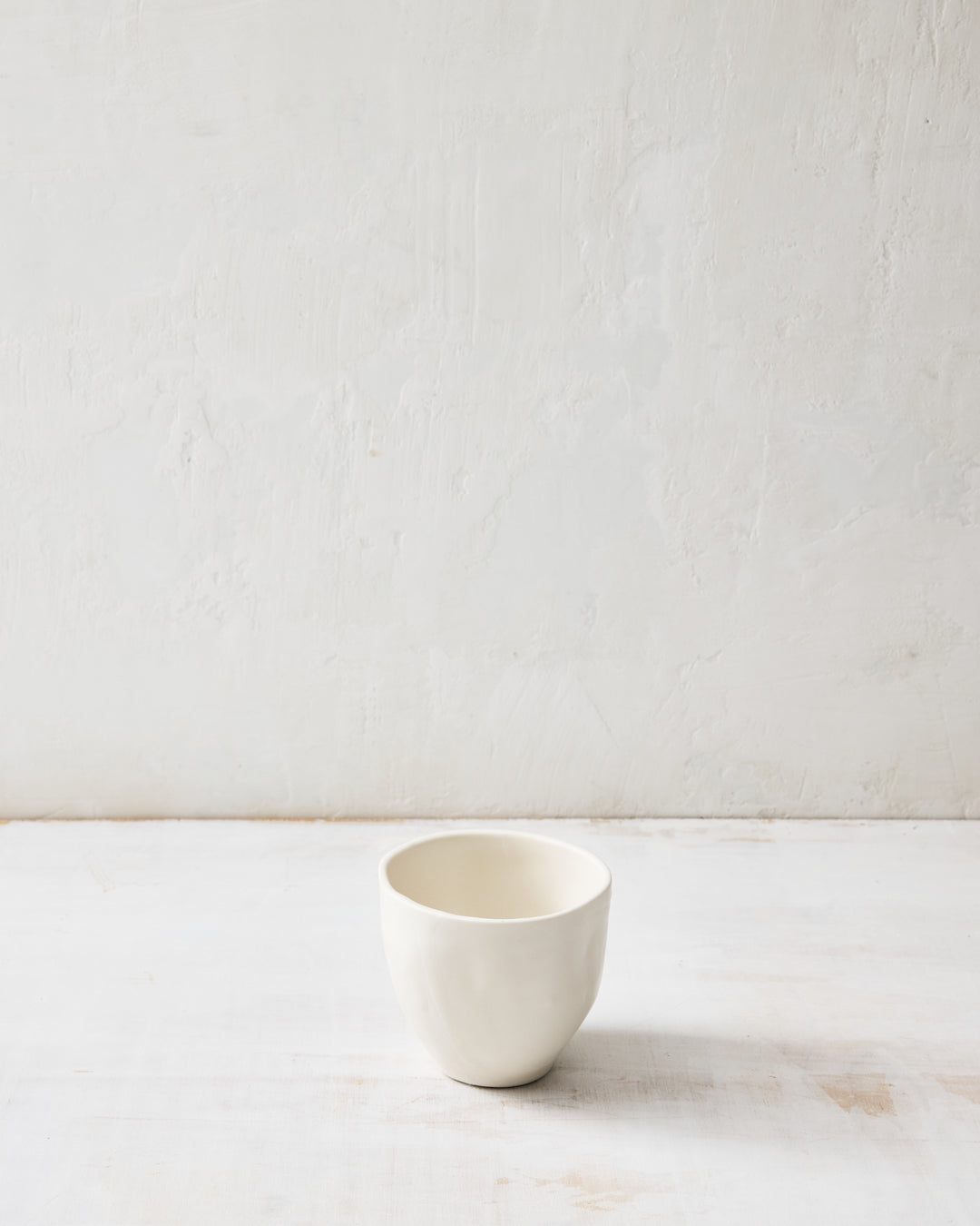DBO HOME Wabi Tea Bowl in Foam glaze, handmade porcelain with a small rounded form, subtle white-on-white layered glaze, and stone-like surface texture, photographed on a whitewashed surface.