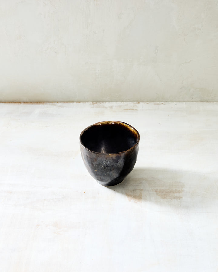 DBO HOME Wabi Tea Bowl in French Roast glaze, handmade porcelain with a small rounded form and stone-like surface texture, photographed on a whitewashed surface.