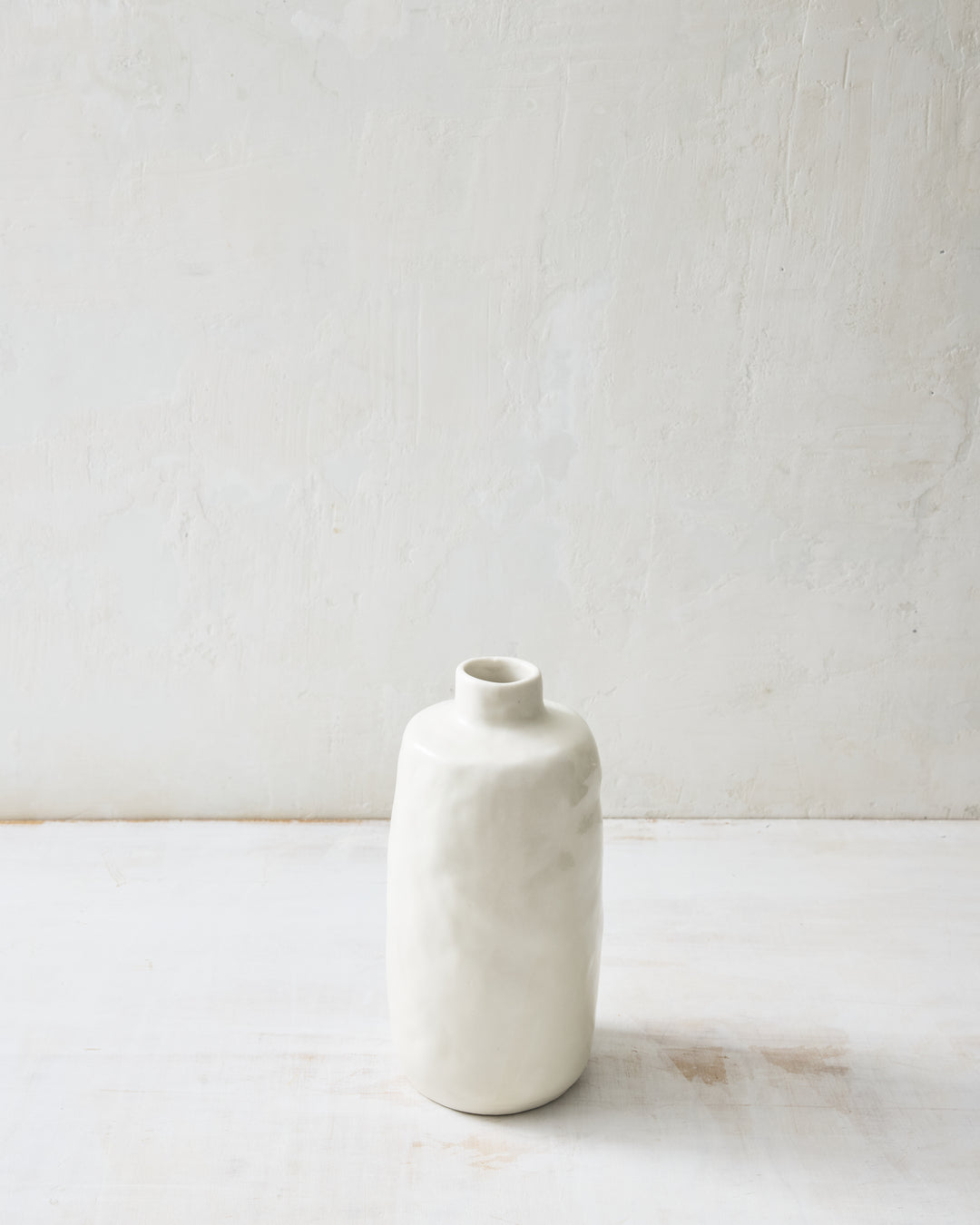 Medium Wabi ceramic vase in Foam glaze with a softly sculpted, hand-formed silhouette and glossy white finish, photographed on a white tabletop against a textured neutral wall.