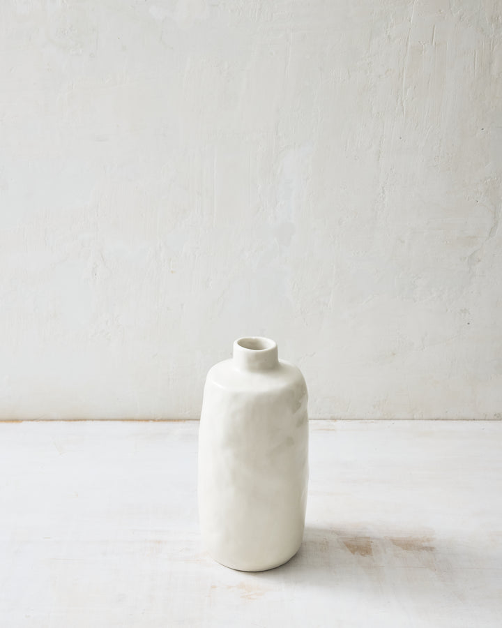 Medium Wabi ceramic vase in Foam glaze with a softly sculpted, hand-formed silhouette and glossy white finish, photographed on a white tabletop against a textured neutral wall.