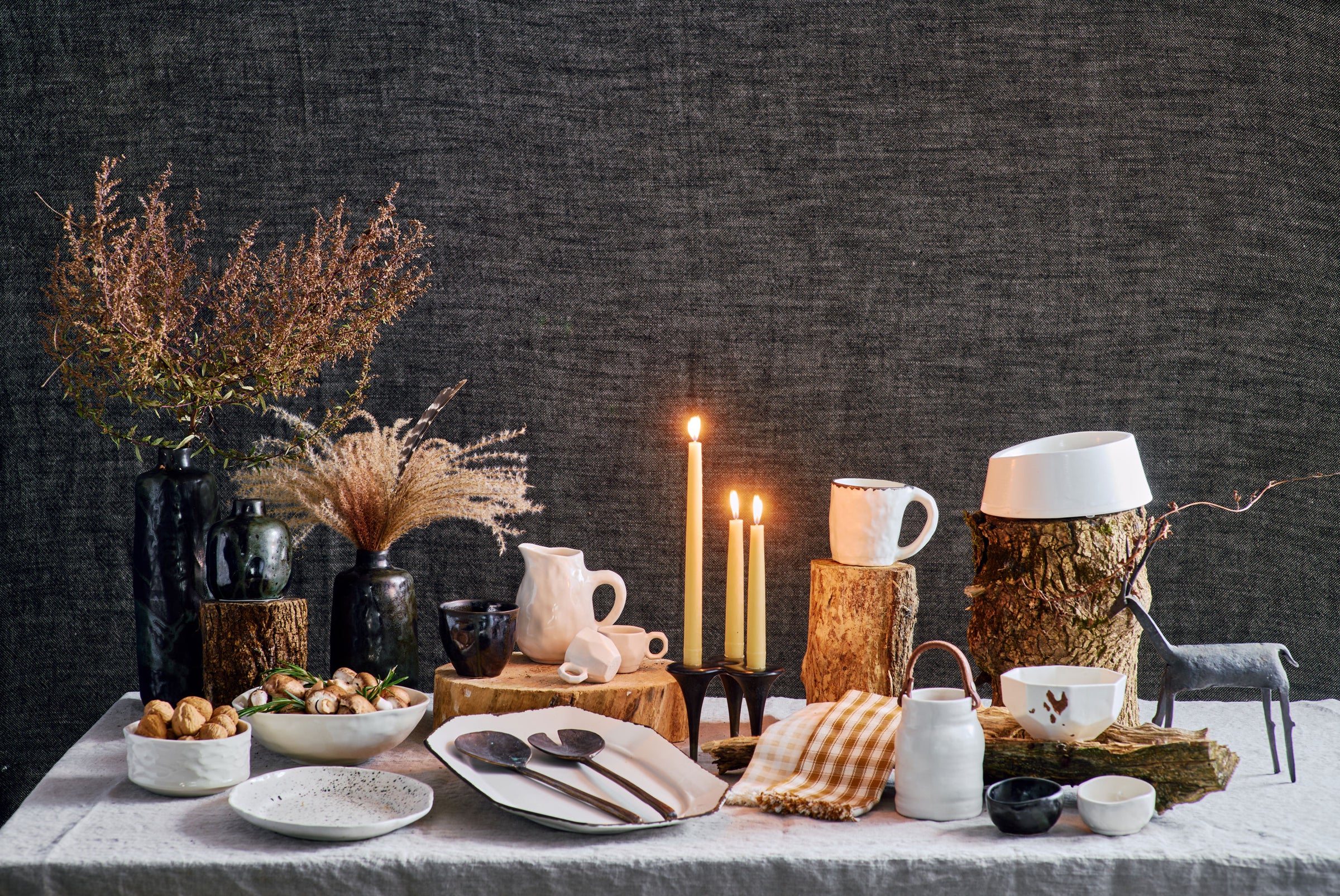 DBO HOME 2023 holiday gift guide spread of everyday luxury handmade ceramic and bronze pieces arranged on an elegant and rustic holiday table with lit candles and wood details