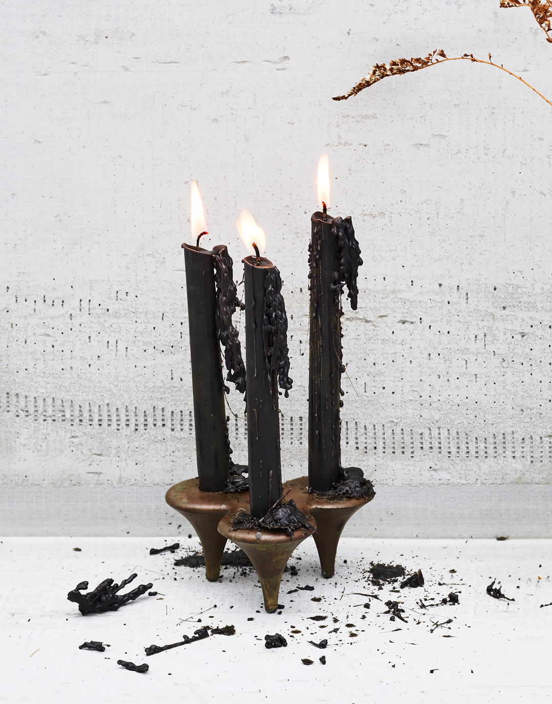 Handcast stake stiletto bronze candlesticks with black candles and dripping black wax on a concrete background