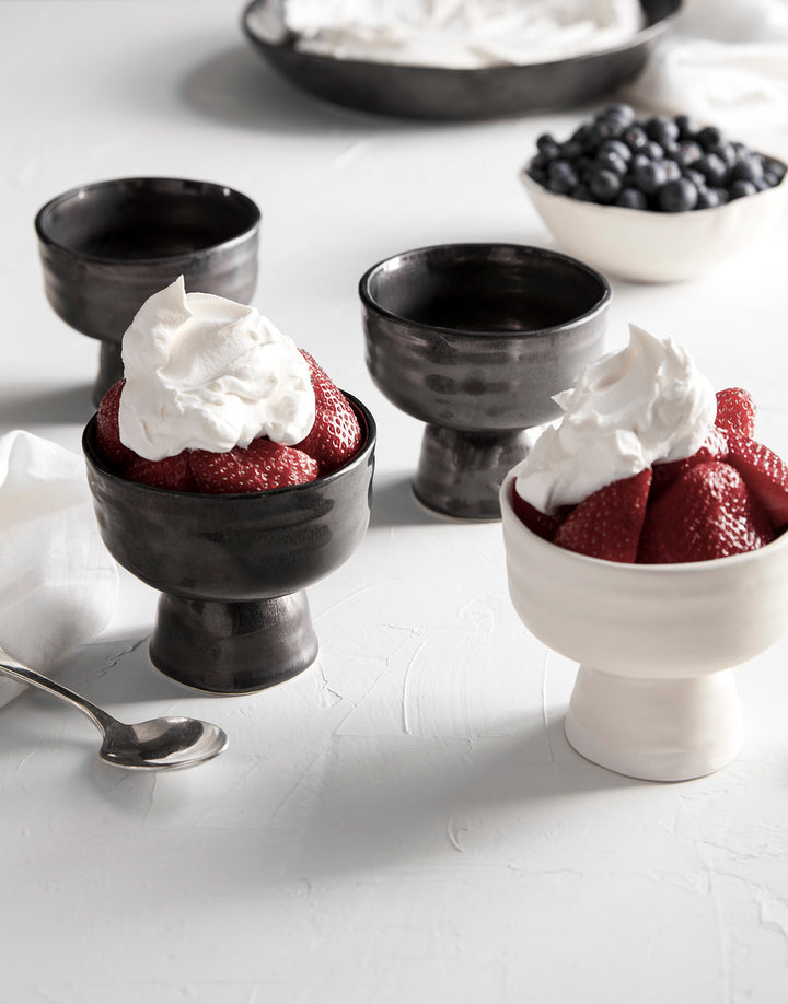 DBO HOME set of artisan ceramic small batch dessert coupe in white and black glaze with stawberries, blueberries, and whipped cream on a white table