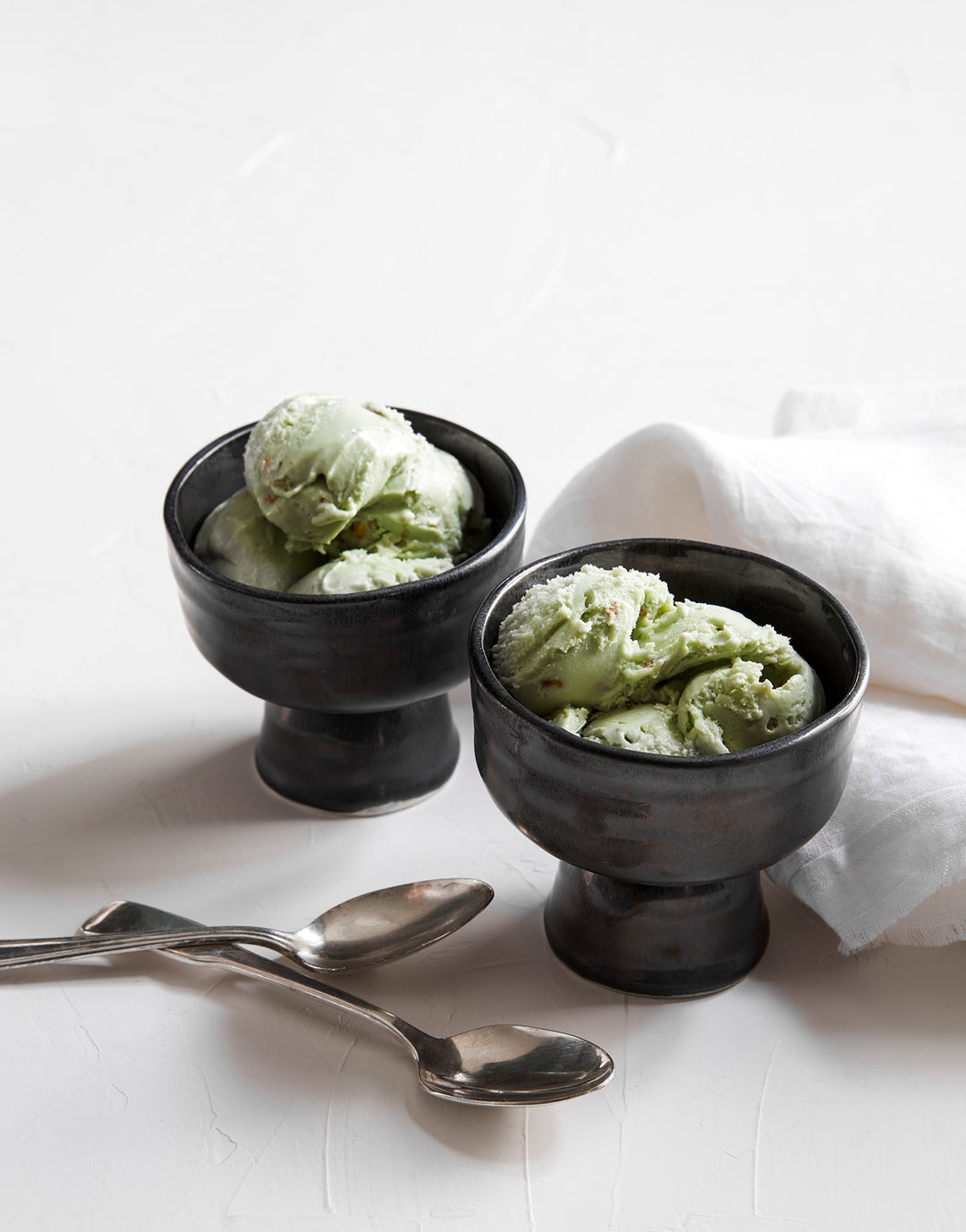 DBO HOME set of artisan ceramic small batch dessert coupe in black glaze with green pistachio ice cream on a white table with white linen napkins