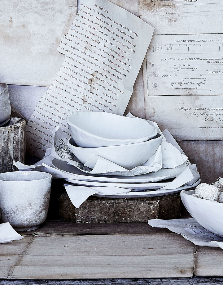Stack of DBO HOME white porcelain handbuilt soup bowls in textured scene with old papers and natural materials