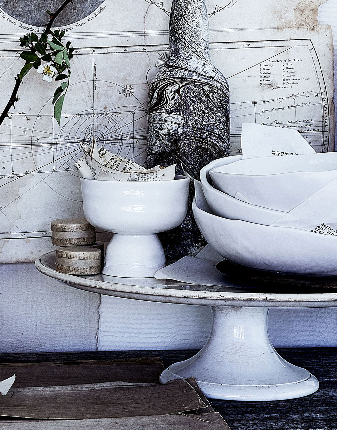 DBO HOME artisan handmade porcelain coupe on cakestand with ceramic bowls and textured vintage map and bottles