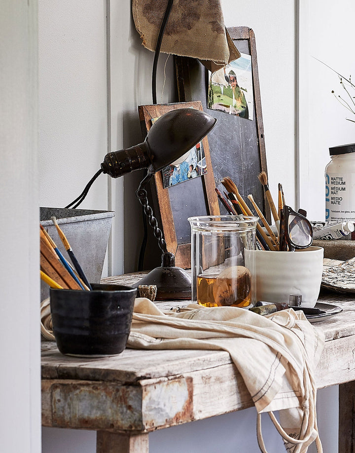 DBO HOME artisan ceramic cups on artist's table filled with paintbrushes and art supplies