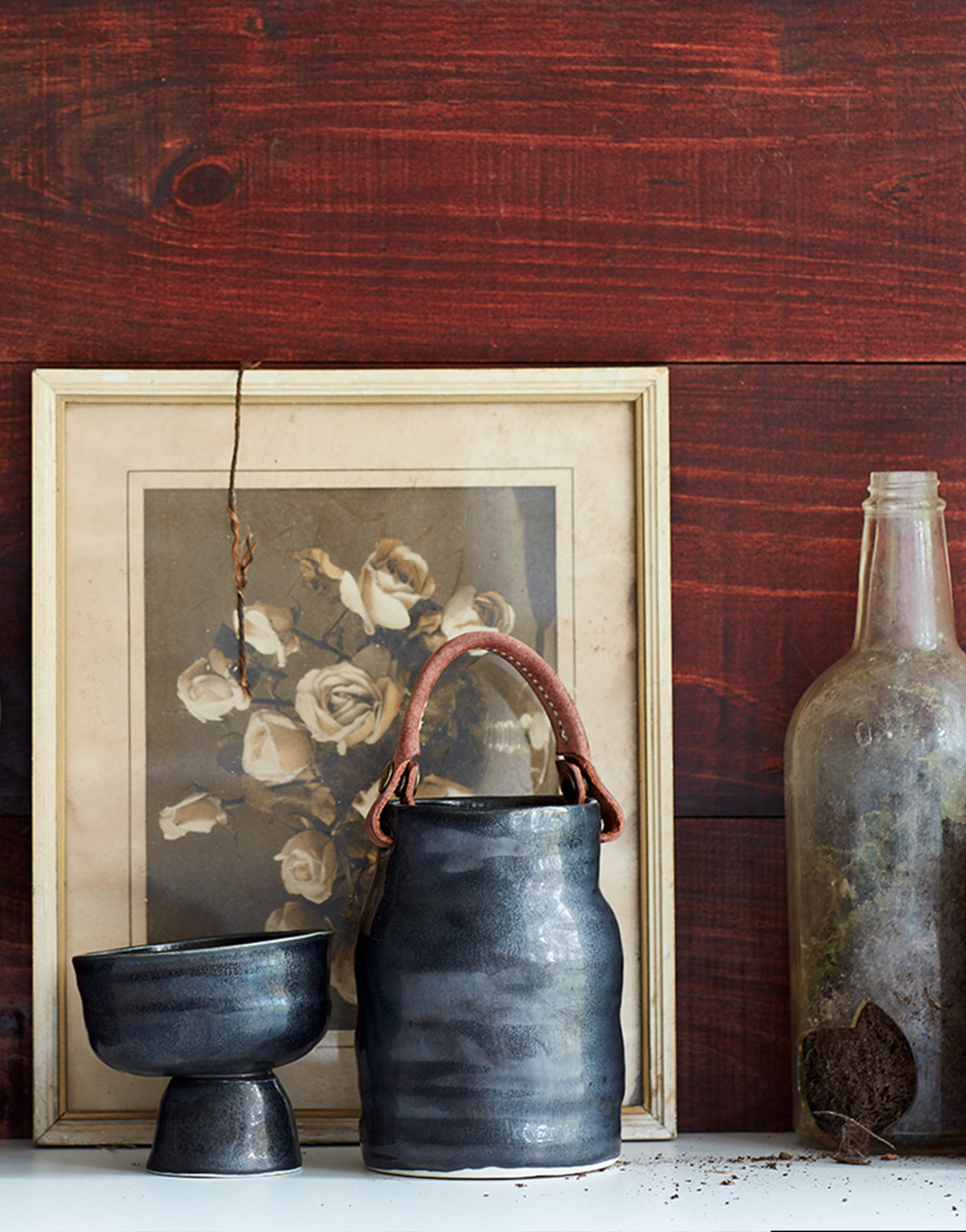 DBO HOME artisan black utility vessel with hand stitched leather handle in front of vintage flower photograph and red wood wall