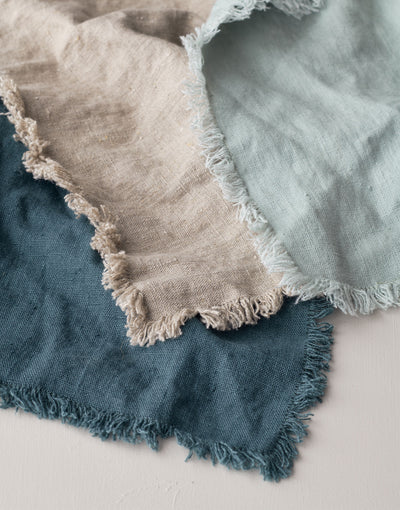 Rustic Linen Napkin Set | Detail image of three square linen napkins layered on a neutral background in a natural linen color, a light peppermint green color, and a deep bluegrass blue 